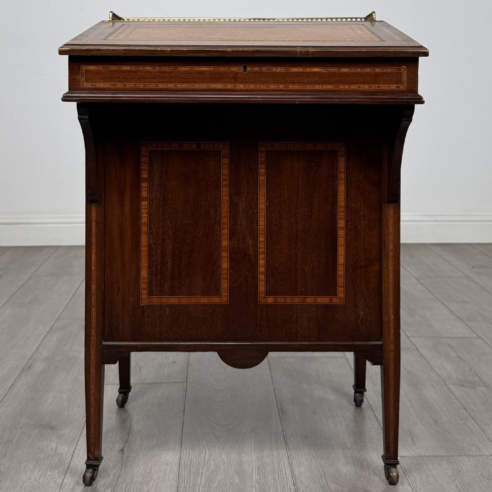 An Edwardian mahogany Davenport desk featuring satinwood crossbanding, a top brass gallery rail, and castors on the base.