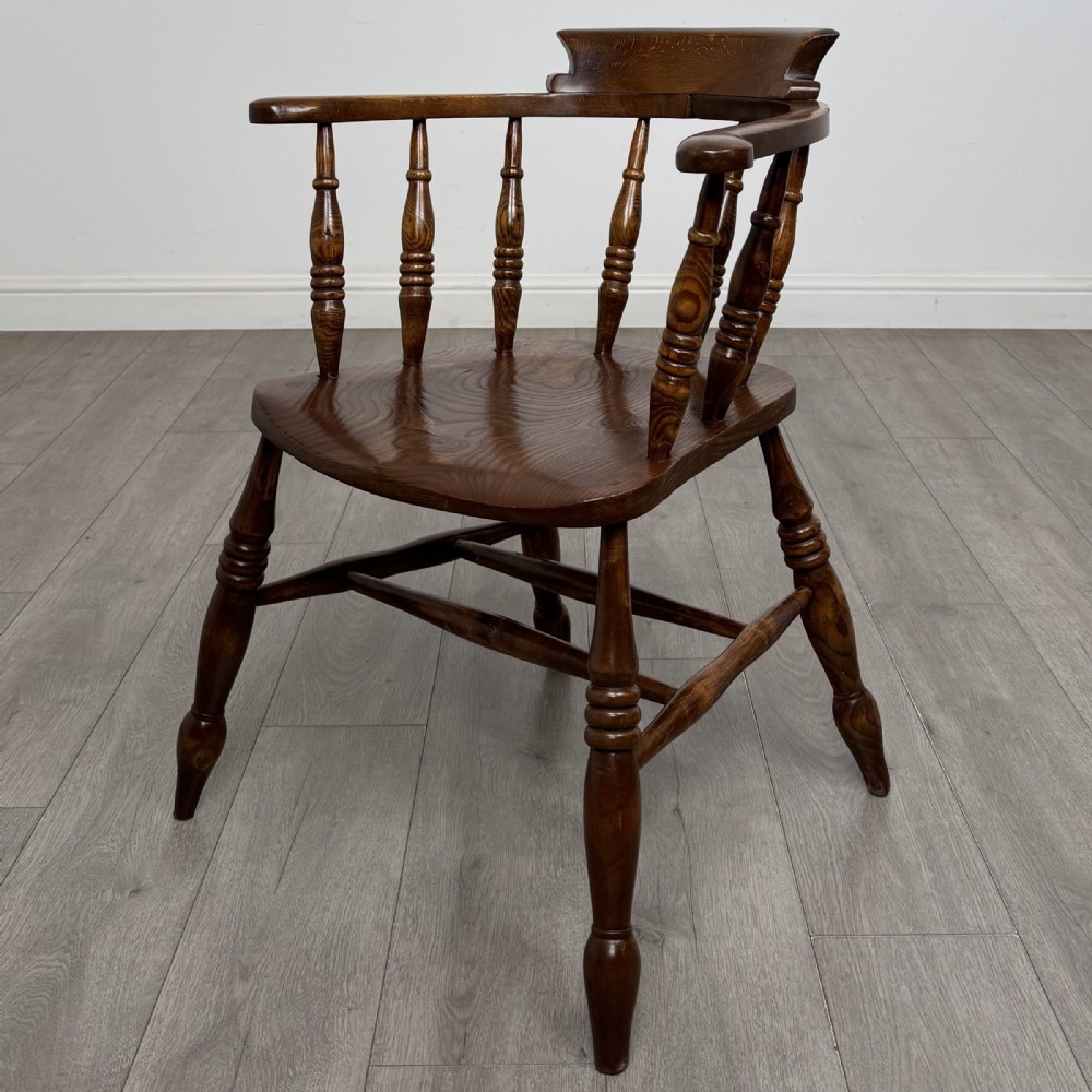 A 20th-century antique elm smokers bow armchair featuring a horseshoe-shaped top rail, turned spindles, a shaped solid elm seat, and turned legs with H-stretchers.