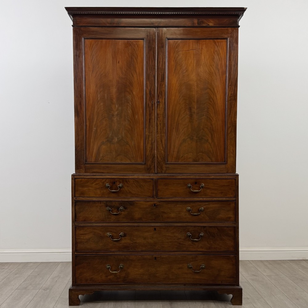 An 18th-century Georgian mahogany linen press featuring flame mahogany door panels above four drawers with brass handles and bracket feet.