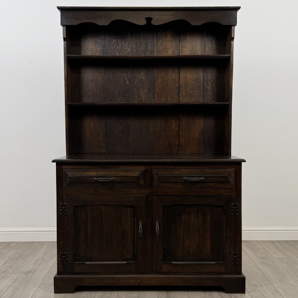 A dark oak Welsh dresser featuring an upper plate rack with open shelves set above a two-drawer, two-door base cabinet.