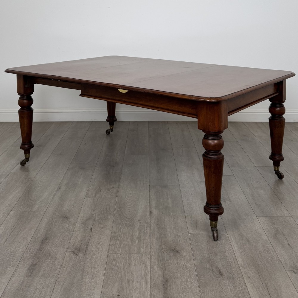 A 19th-century Victorian mahogany dining table featuring turned legs fitted with brass castors and a rectangular top with rounded corners.
