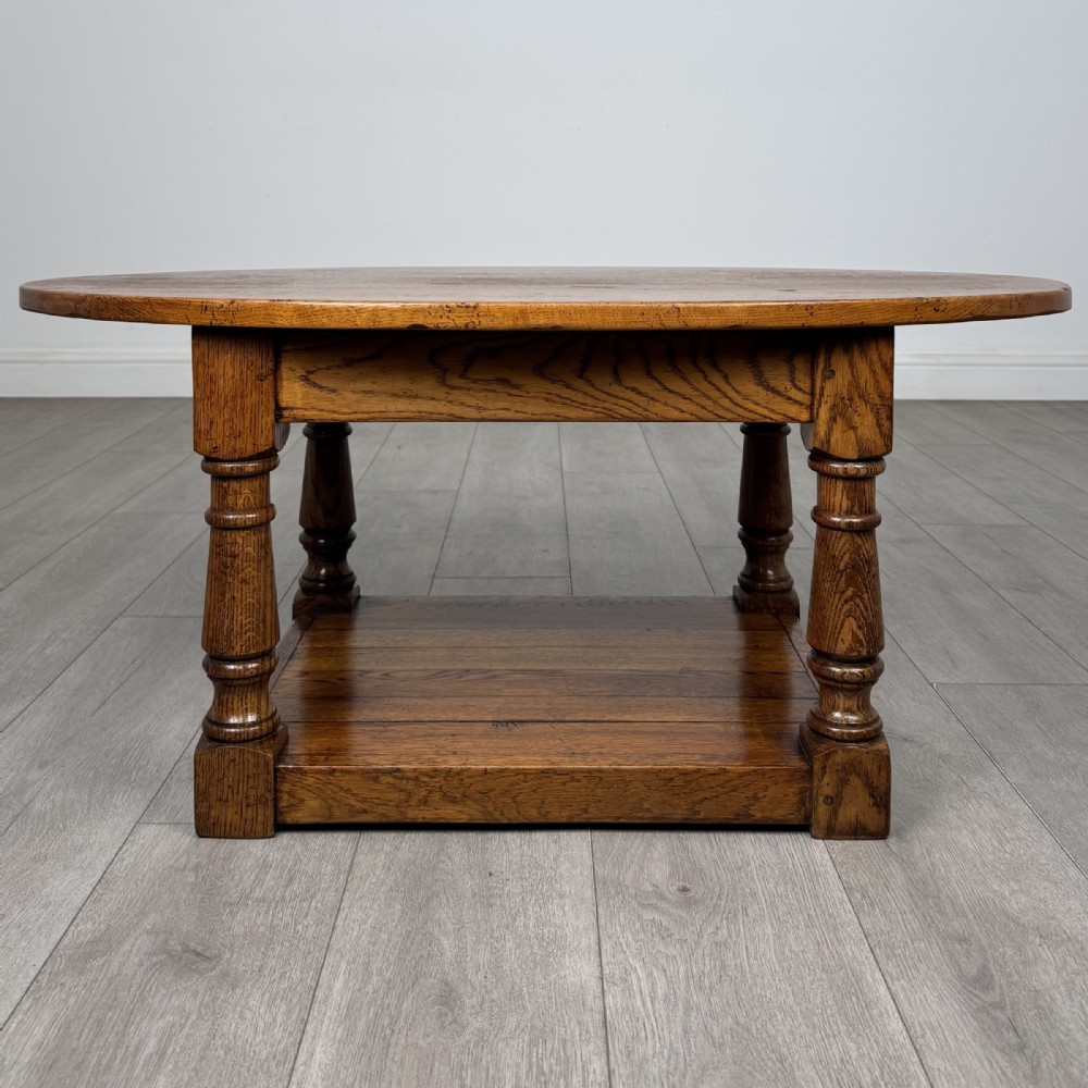 An antique oval oak coffee table featuring four turned baluster legs and a solid lower undertier shelf.