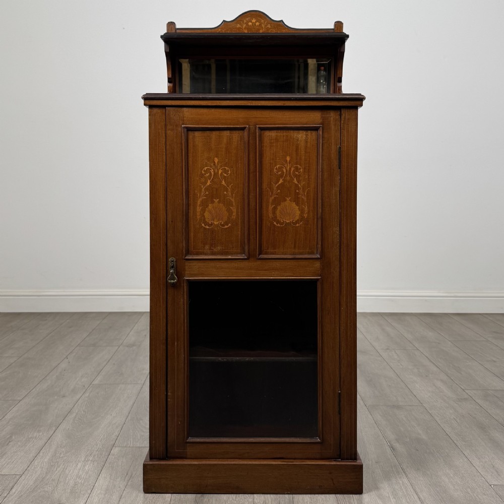 An Edwardian inlaid mahogany cabinet featuring an upper mirrored gallery, two marquetry panels with shell motifs, and a glazed lower door section.