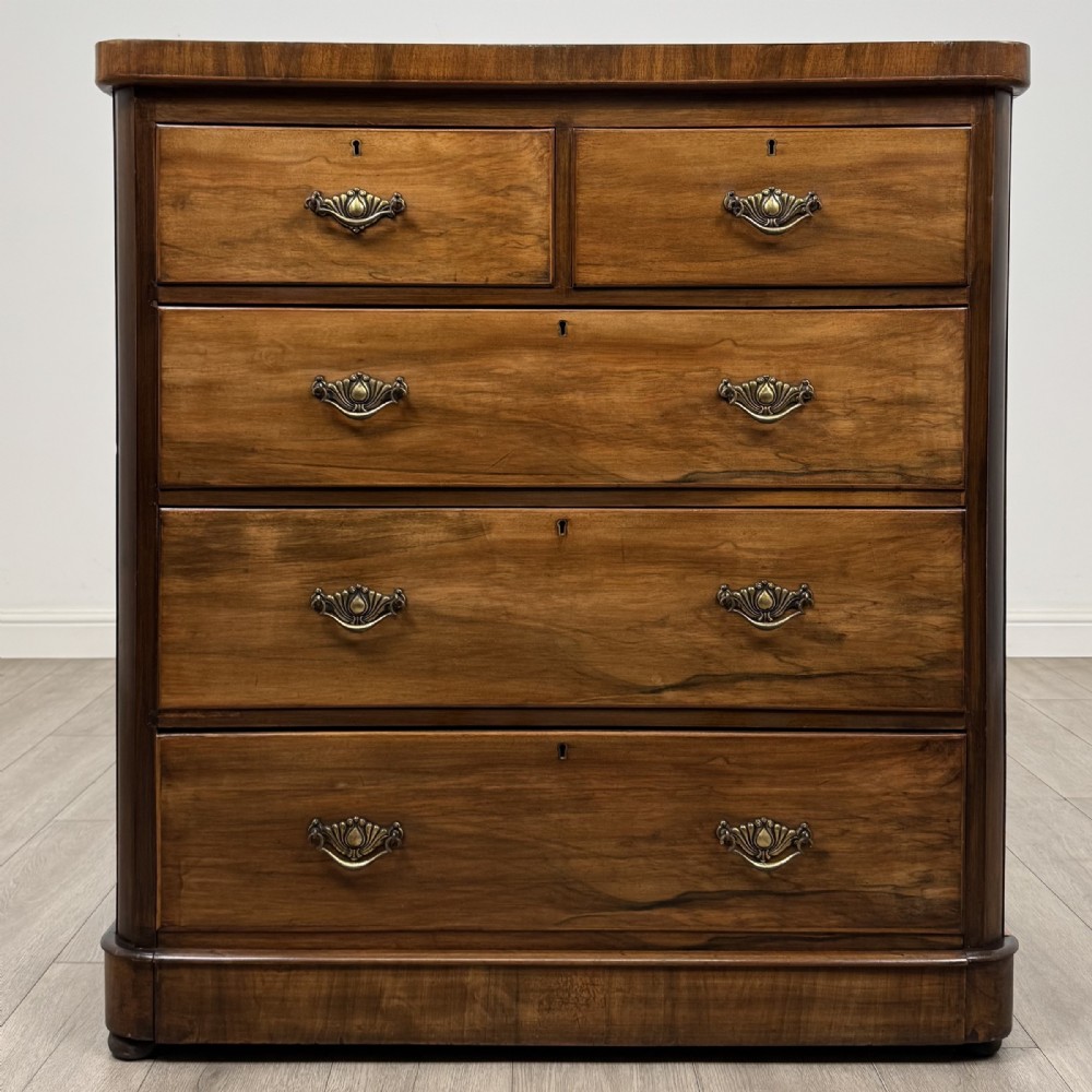 An Edwardian walnut chest of drawers featuring two short drawers over three long drawers with ornate brass handles.