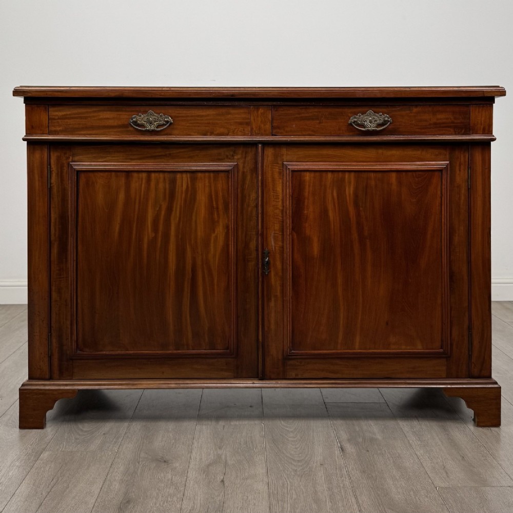 A Victorian mahogany cupboard featuring two drawers with brass drop handles above two panelled doors, resting on bracket feet.