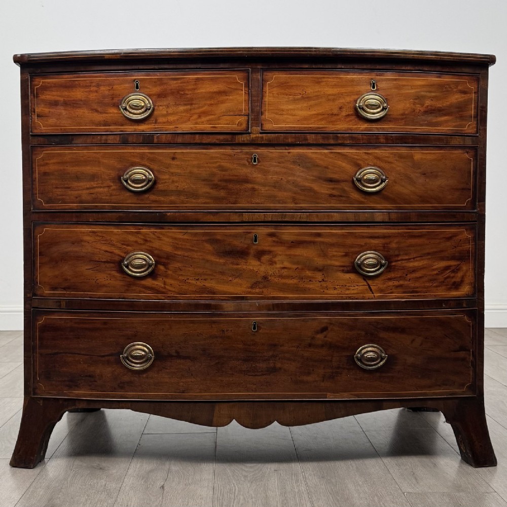 An eighteenth-century Georgian bow-fronted mahogany chest of drawers with stringing inlay, oval brass handles, and splayed bracket feet.