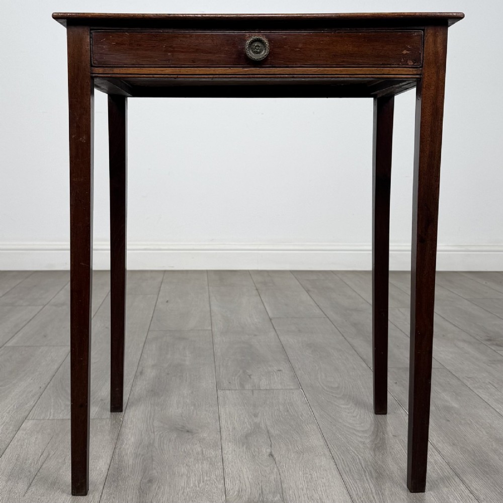 An 18th-century Georgian mahogany side table with a single shallow drawer featuring a central circular brass pull, supported by four slim tapered legs.