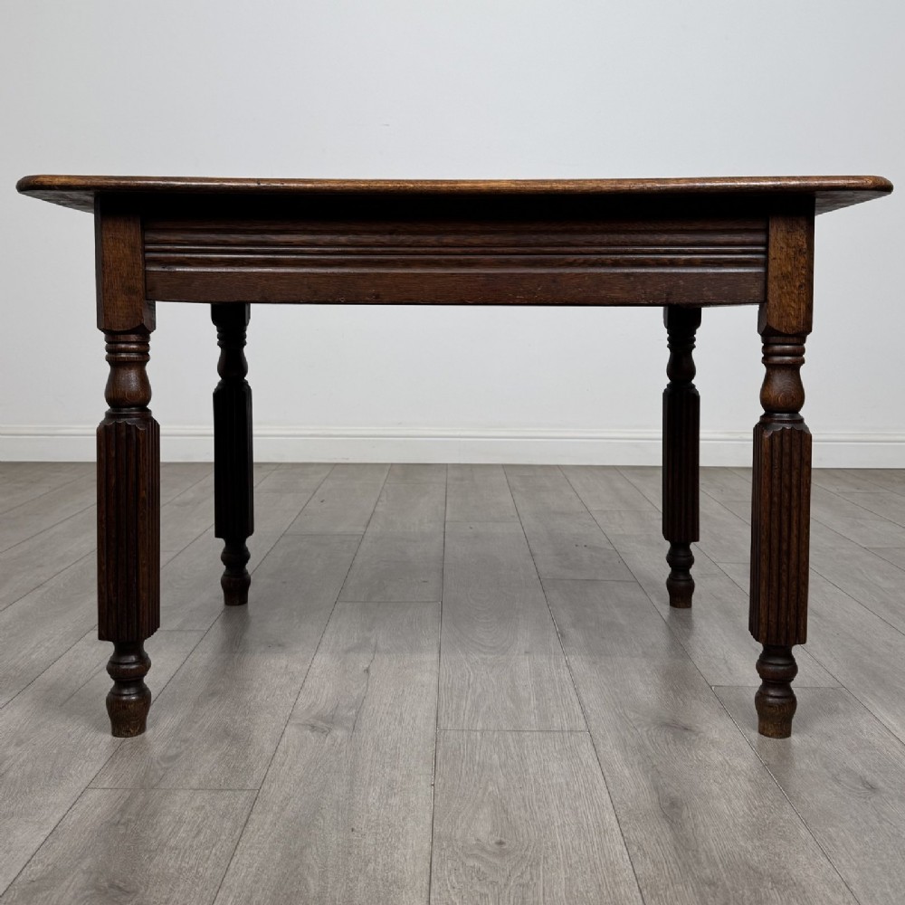 An antique dark oak writing table featuring a rectangular top, moulded apron, and four turned reeded legs.