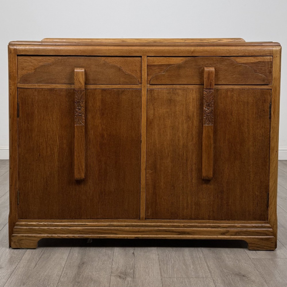 A medium brown oak Art Deco sideboard featuring two drawers over two cabinet doors with long vertical carved wooden handles.
