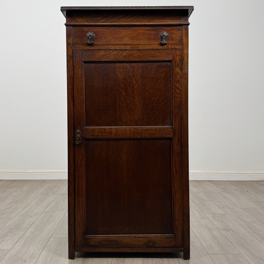A tall dark oak Edwardian storage cupboard featuring a lift-up top lid, panelled single door, and dark metal hardware.