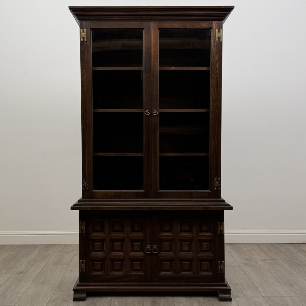 A dark brown oak display cabinet featuring two glazed upper doors over two lower doors with carved geometric panels.