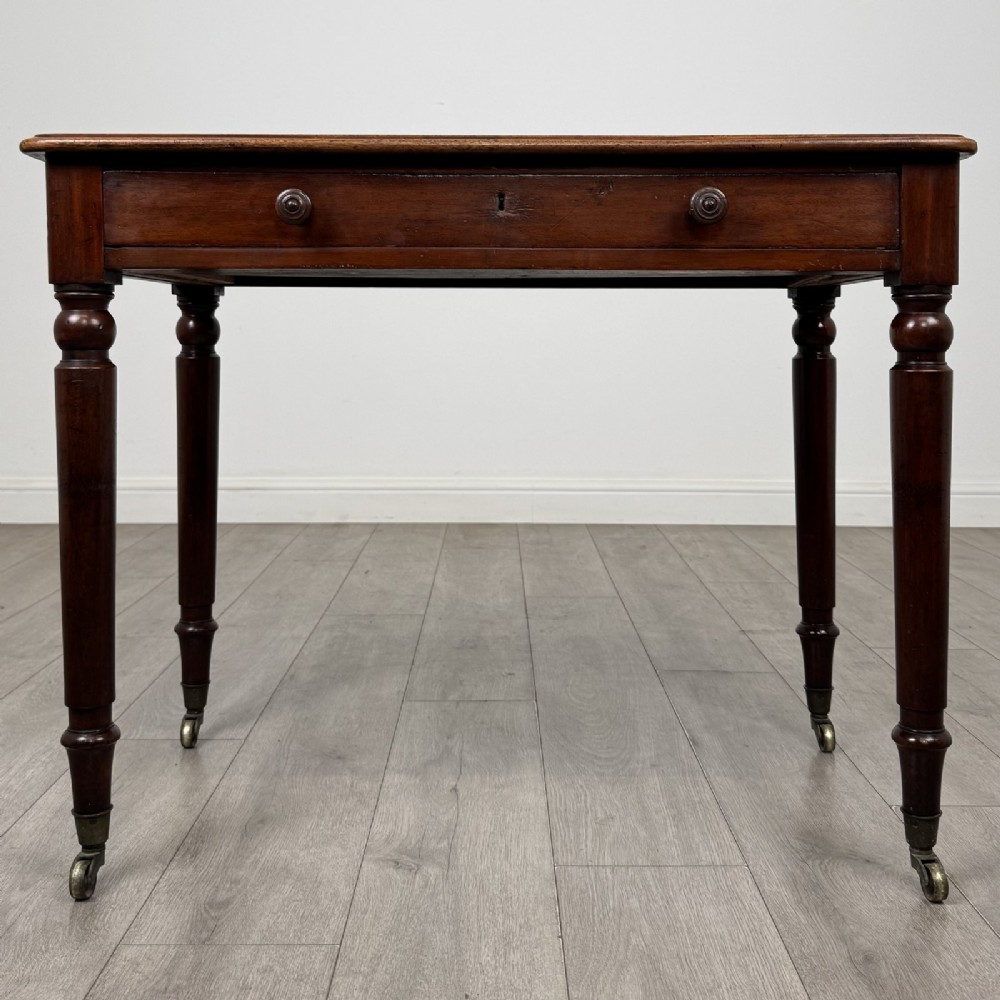 Victorian mahogany writing table featuring a single frieze drawer with turned wooden knobs and four turned legs on brass castors.