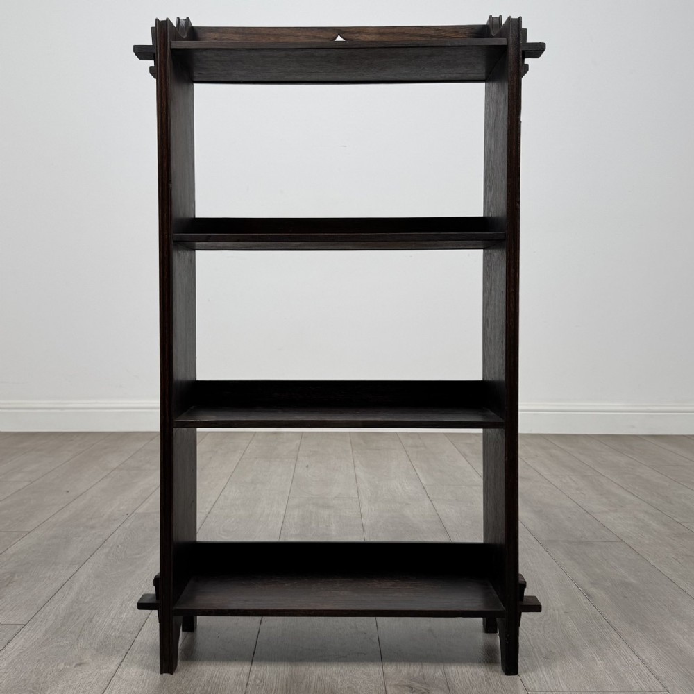 A compact dark oak open bookcase featuring four tiered shelves, side uprights with exposed tenon projections, and a low top gallery rail.