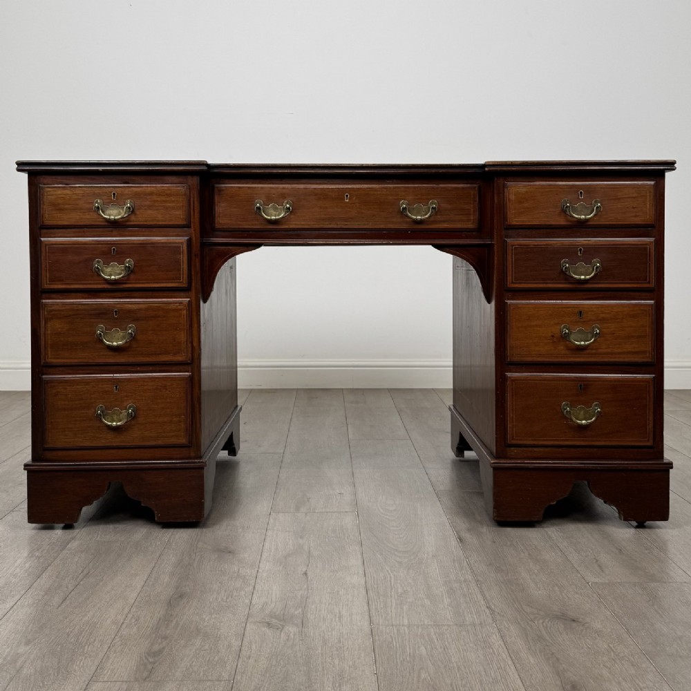 A Victorian mahogany pedestal desk featuring a breakfront design, nine drawers with inlaid border details, brass swan-neck handles, and bracket feet.