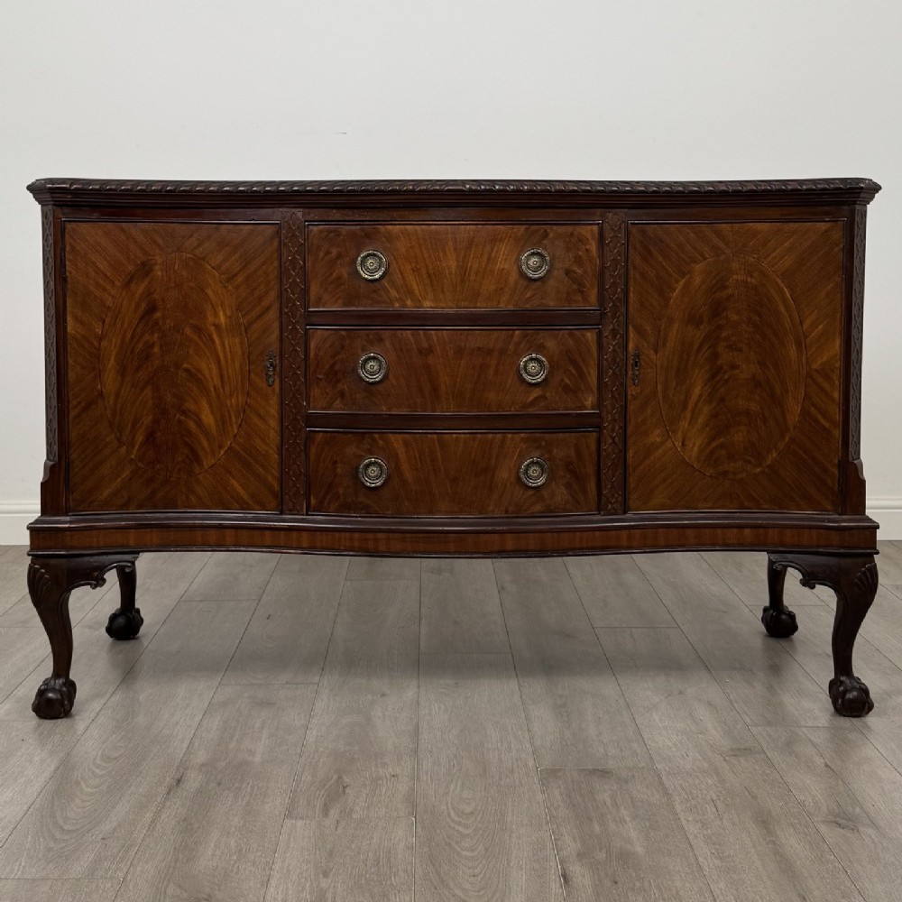 An Edwardian mahogany sideboard with three central drawers flanked by cupboard doors featuring oval mahogany veneers and carved cabriole legs terminating in ball-and-claw feet.