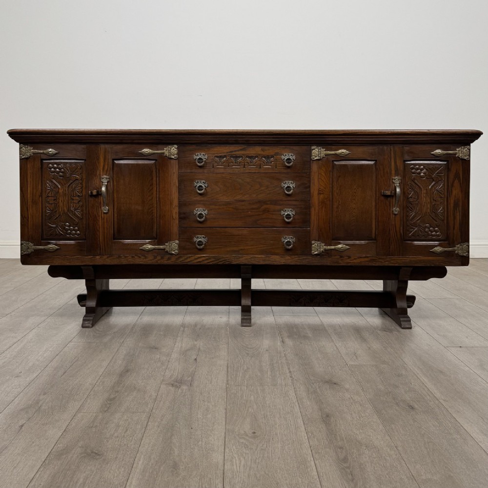 A large dark oak sideboard featuring carved panel doors, central drawers, decorative metal hinges, and a stretcher base.