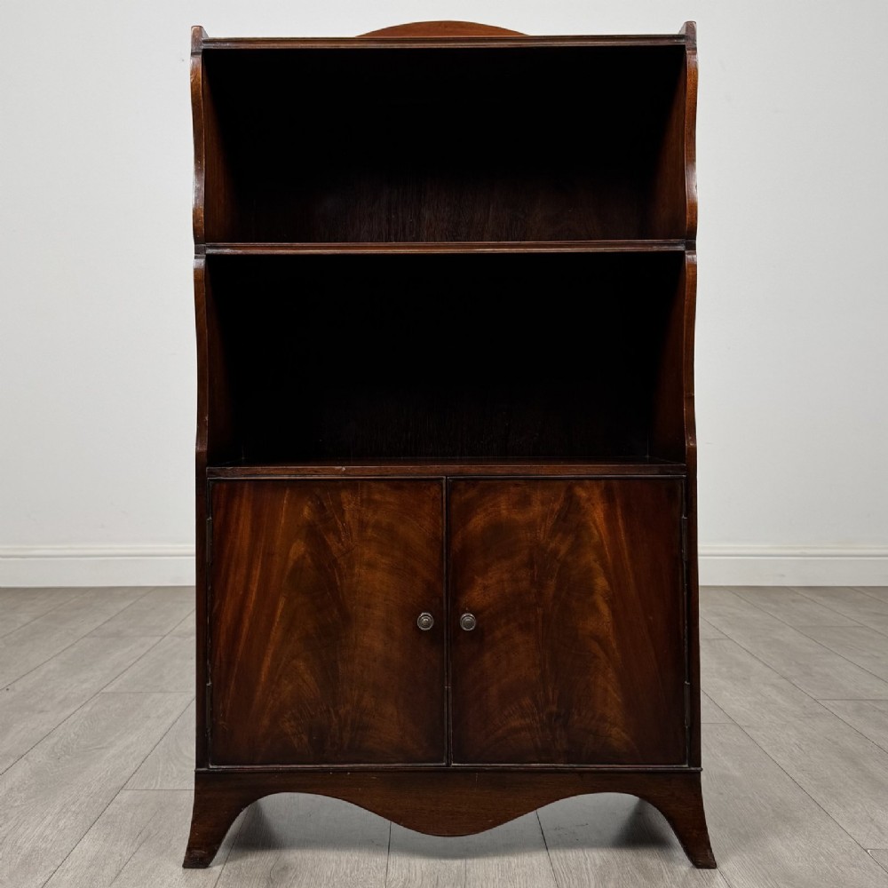 An antique mahogany open bookcase featuring a shaped raised gallery top, two upper shelf spaces, and a lower two-door cabinet with flame mahogany veneered panels.
