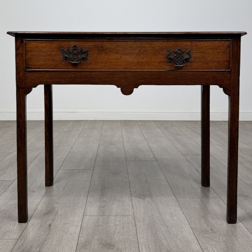An 18th-century Georgian dark oak side table featuring a single drawer with pierced brass handles and straight square legs.
