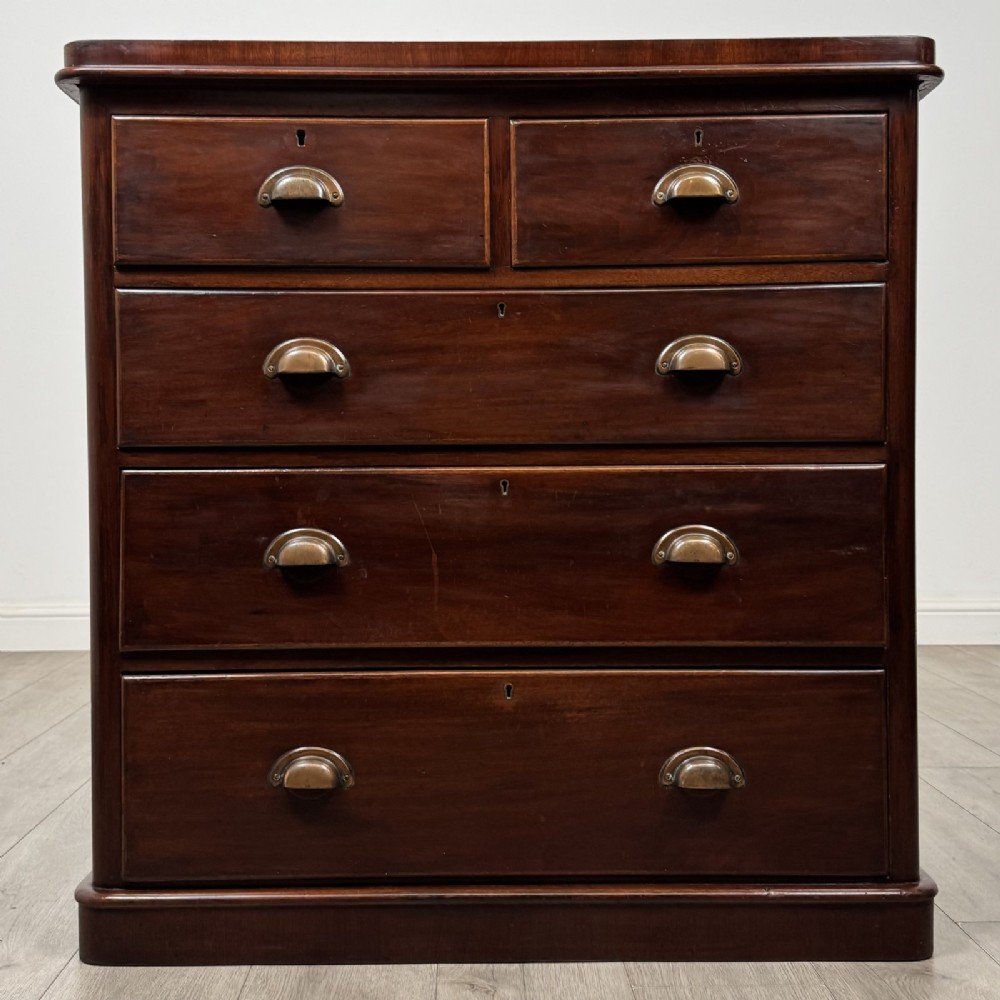 A Victorian mahogany chest of drawers featuring a two-over-three drawer configuration, brass cup handles, and a plinth base.