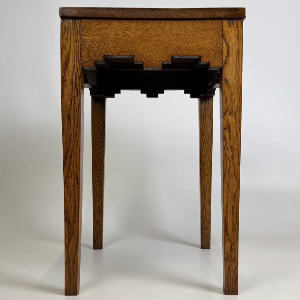 A tall, slender Arts and Crafts golden oak side table featuring tapered square legs and a notched, stepped apron.