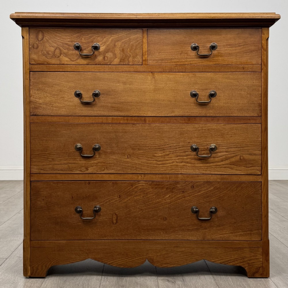 An antique ash chest of drawers featuring a two-over-three drawer configuration with drop handles and a shaped lower apron.