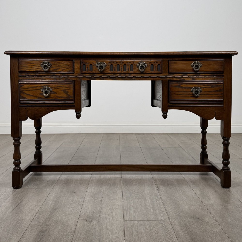 An antique dark oak writing desk featuring five carved drawers with metal drop handles, turned legs, and lower stretchers.