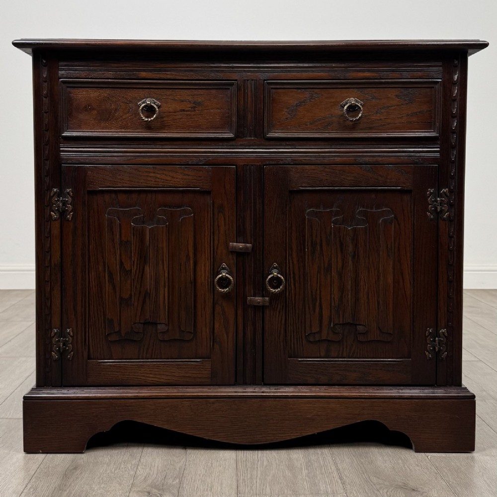 A dark brown oak storage cupboard featuring two top drawers above twin doors with carved linenfold panels and brass handles.