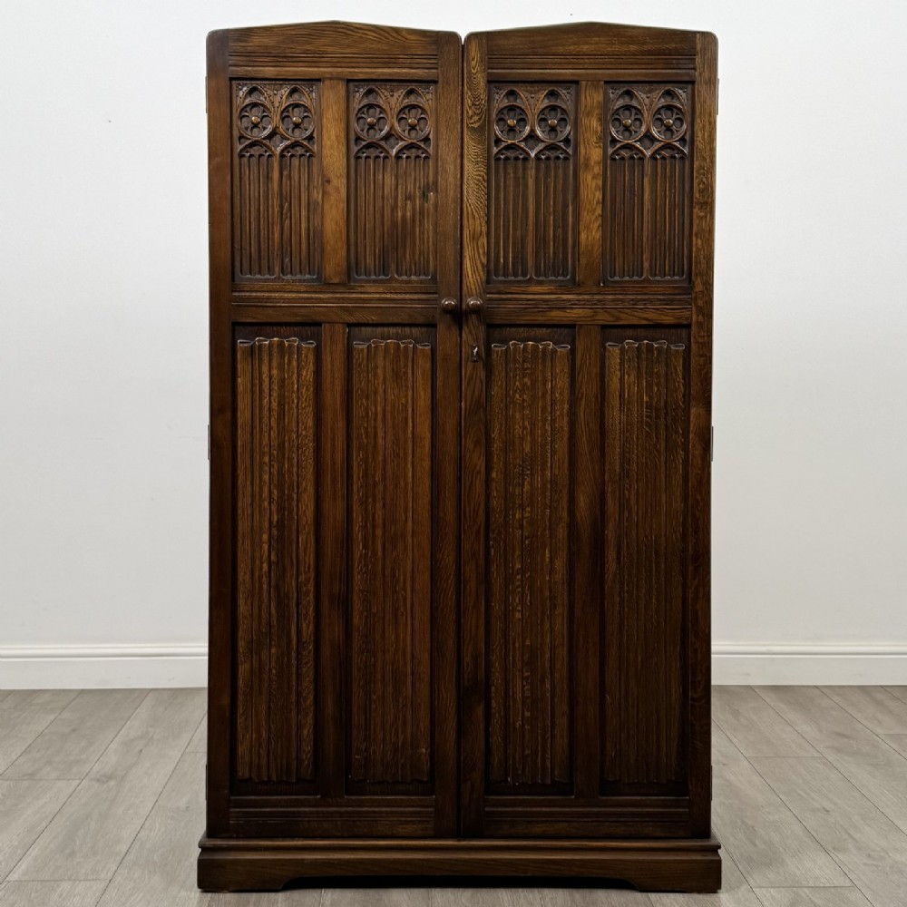 A tall dark brown oak double wardrobe featuring hand-carved Gothic tracery panels on top and vertical panel detail below.