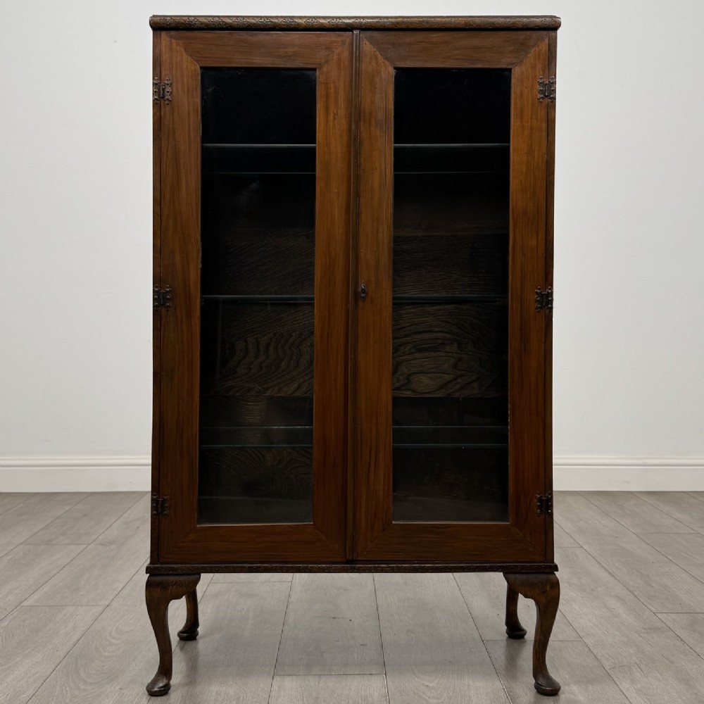 An antique Edwardian mahogany display cabinet featuring twin glazed doors, glass interior shelving, and cabriole legs.