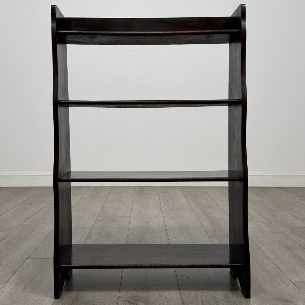 A dark brown Edwardian oak open bookcase featuring four open shelf tiers and shaped side panels.