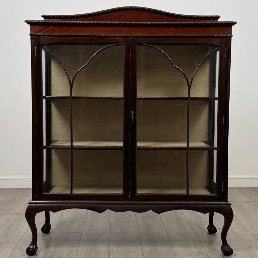 An Edwardian dark mahogany display cabinet with twin astragal glazed doors, fabric-lined interior shelves, and cabriole legs with carved claw and ball feet.