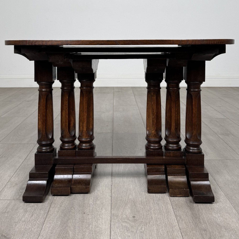 A set of three nesting dark oak occasional tables featuring turned baluster legs and trestle feet.