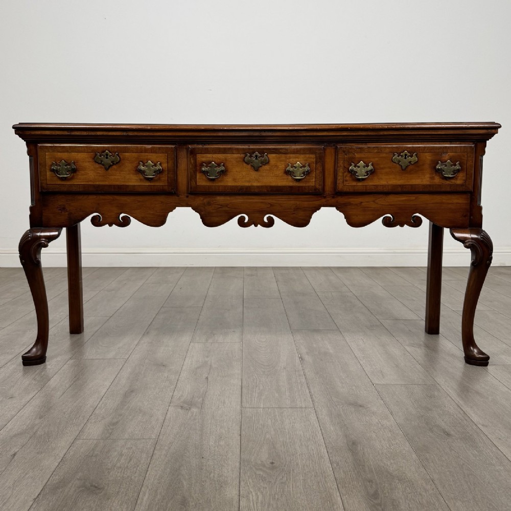 A Queen Anne style elm dresser base featuring three drawers with brass handles, a shaped apron, and cabriole legs ending in pad feet.