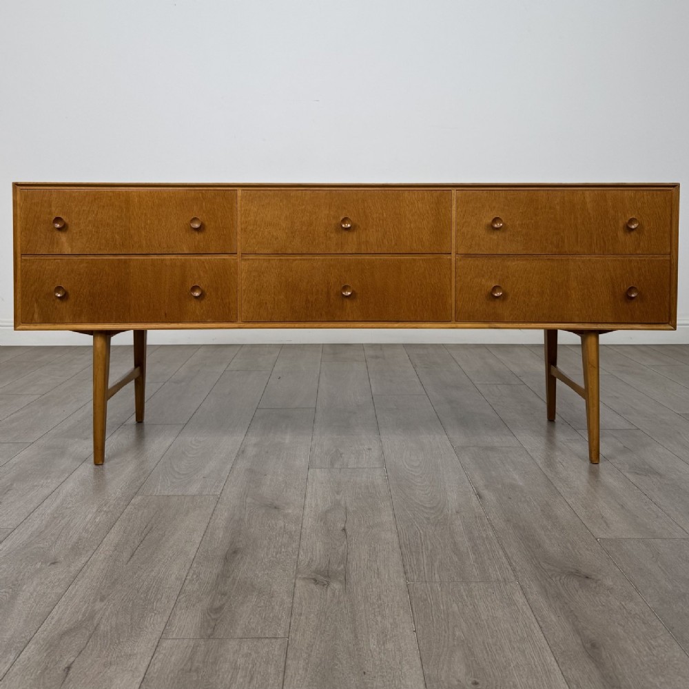 A mid-century oak sideboard featuring six wide drawers with circular wooden pull knobs, supported by tapered legs and side stretchers.