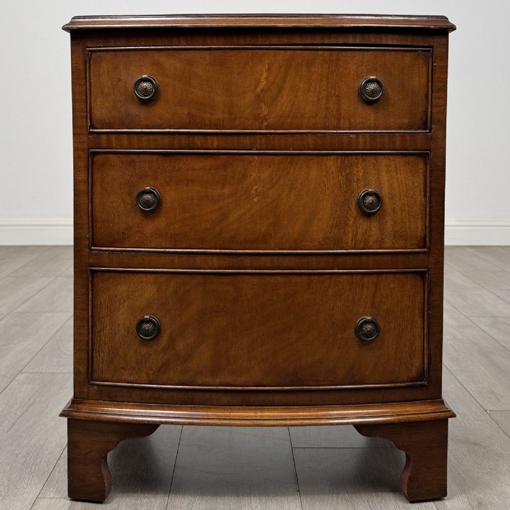 A small antique mahogany bow front chest featuring three drawers with brass ring drop handles resting on bracket feet.