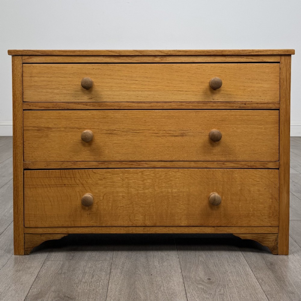 A golden oak chest of drawers featuring three horizontal drawers with turned wooden knob handles resting on a shaped apron base.