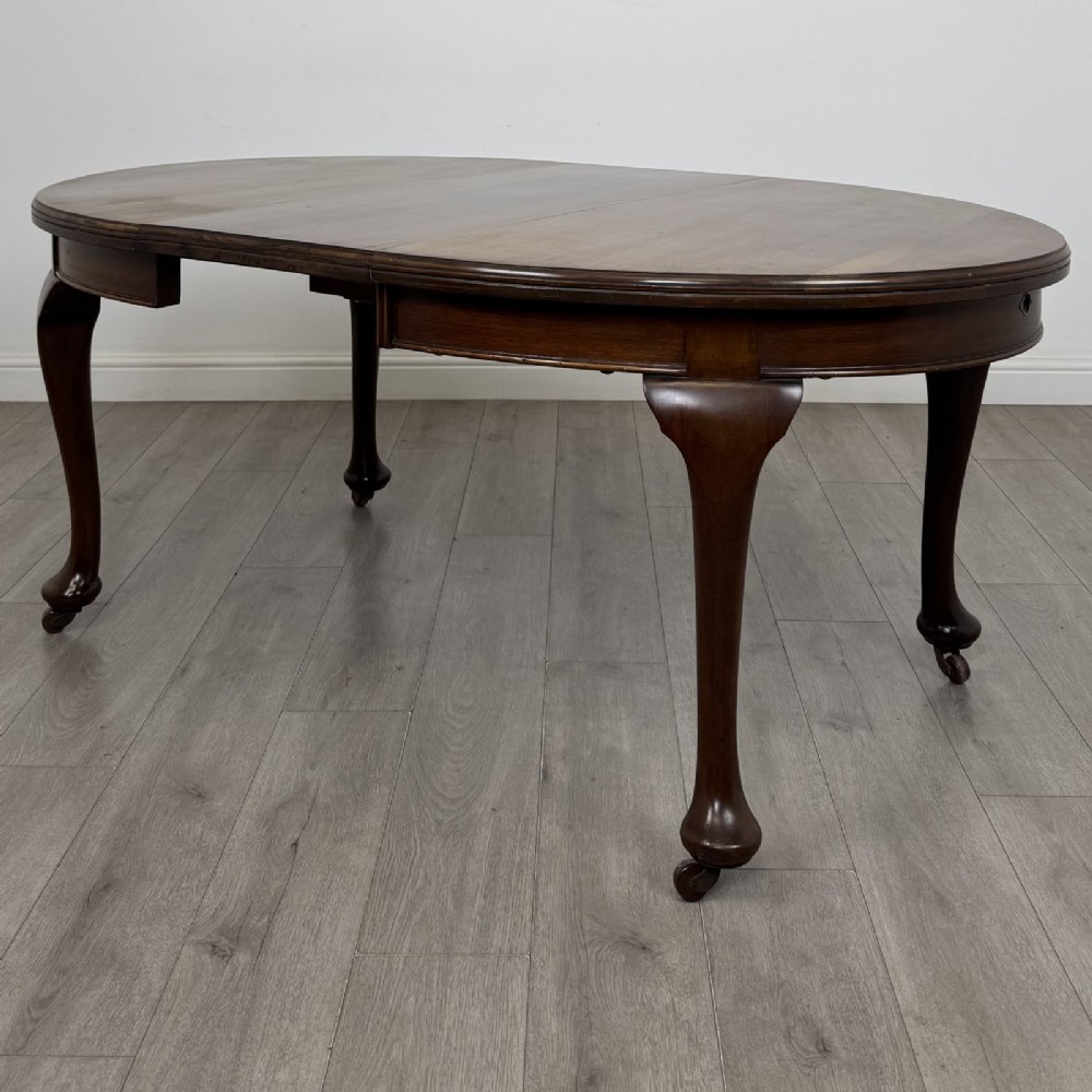 An antique Edwardian oval mahogany extending dining table featuring cabriole legs on castors with a removable centre leaf.