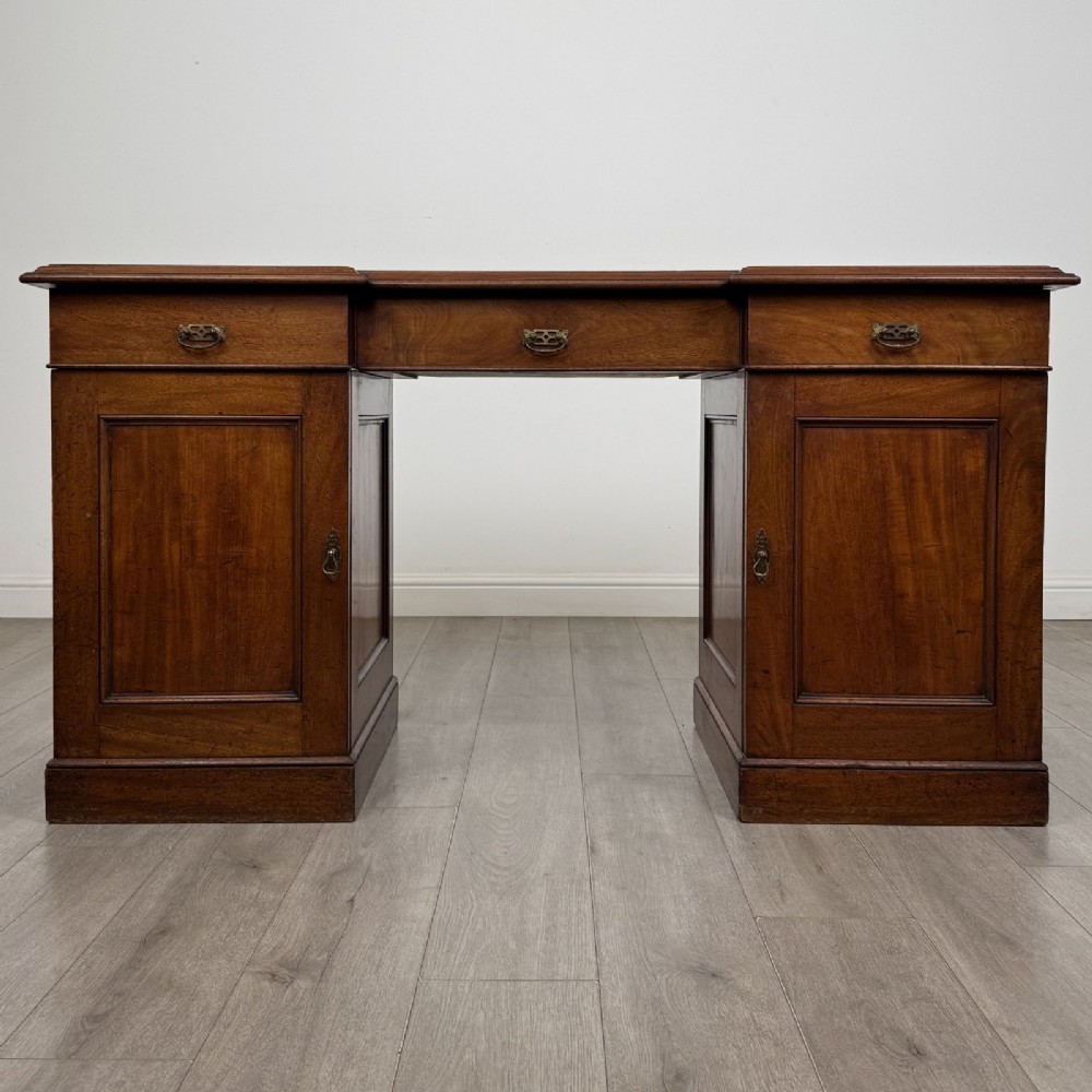 A Victorian mahogany twin pedestal desk featuring a breakfront top, three upper frieze drawers, and two panelled cupboard doors on a plinth base.