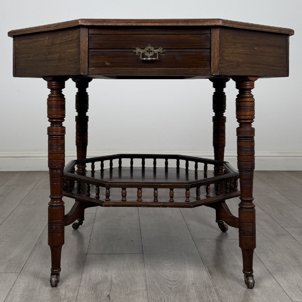 An antique dark mahogany octagonal centre table featuring a drawer with a brass drop handle, ring-turned legs on brass castors, and an octagonal lower shelf with a spindle gallery.