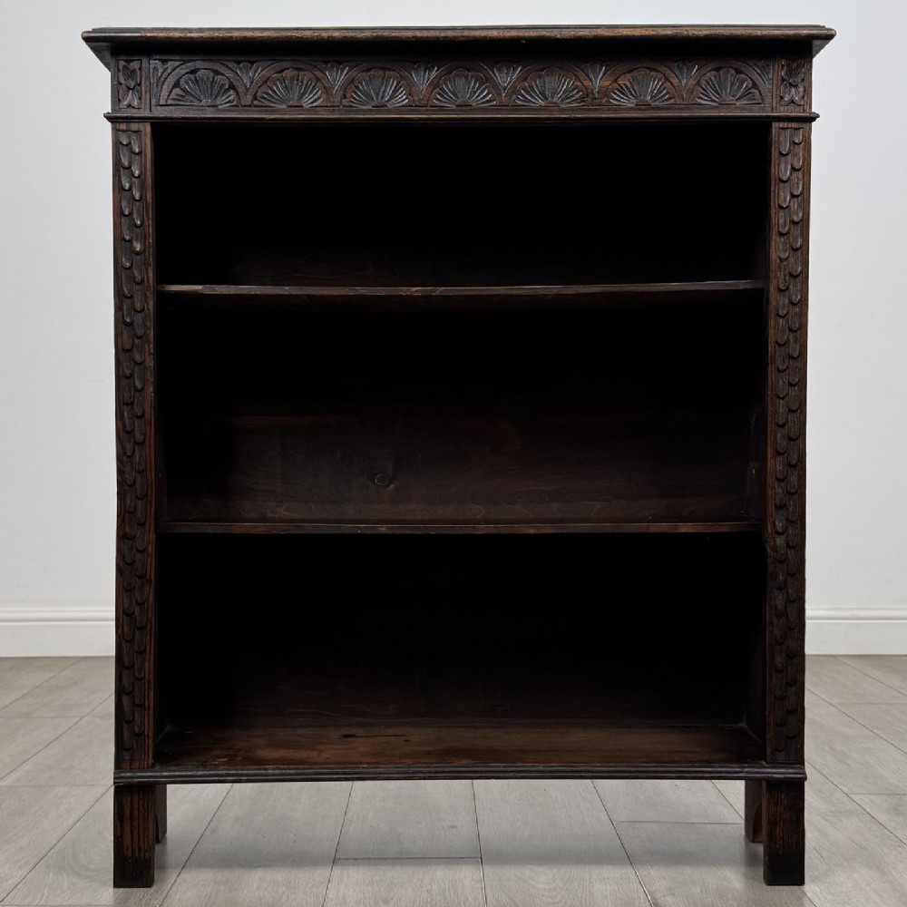 A dark brown Victorian carved oak open bookcase with three adjustable shelves and carved decorative borders on the frieze and uprights.