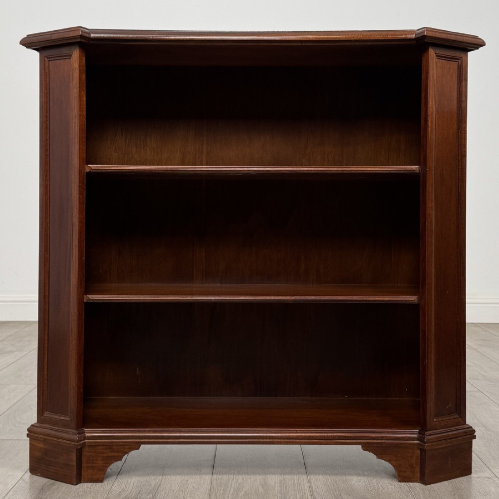 An antique mahogany low open bookcase featuring canted corner posts, three tiers of open shelving, and a shaped bracket foot base.