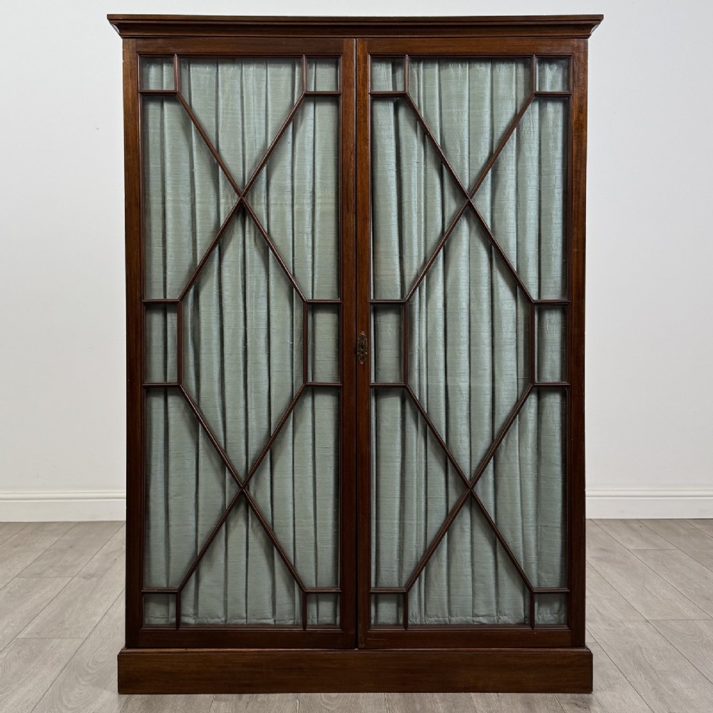 A Georgian style dark mahogany display cabinet featuring two glazed doors with geometric astragal glazing bars and interior green silk lining.