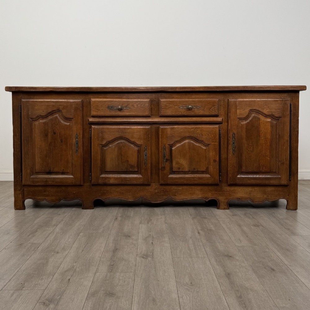 A wide medium brown oak sideboard featuring four arched panel doors, two central drawers, decorative metal hardware, and a shaped apron.