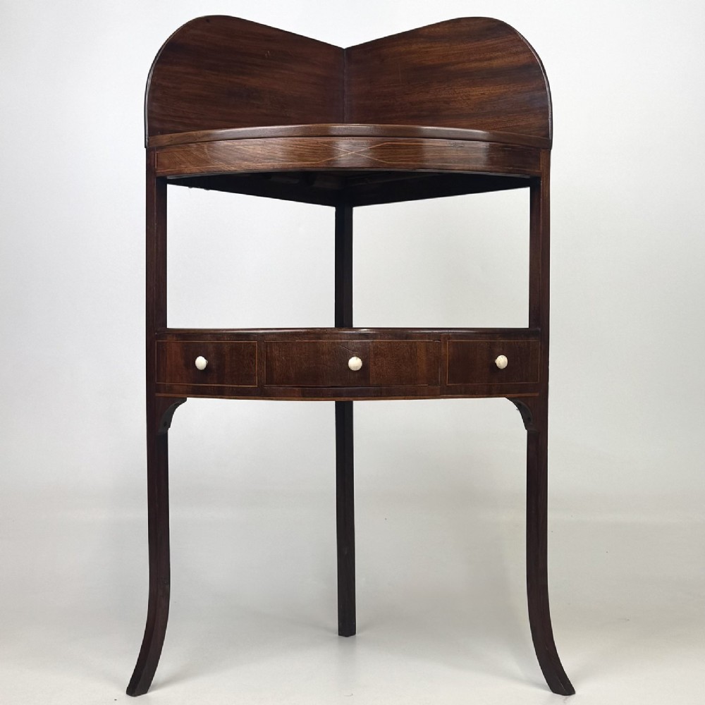 A Georgian style mahogany corner stand featuring a curved raised gallery, inlaid drawer, white handles, and slender splayed legs.