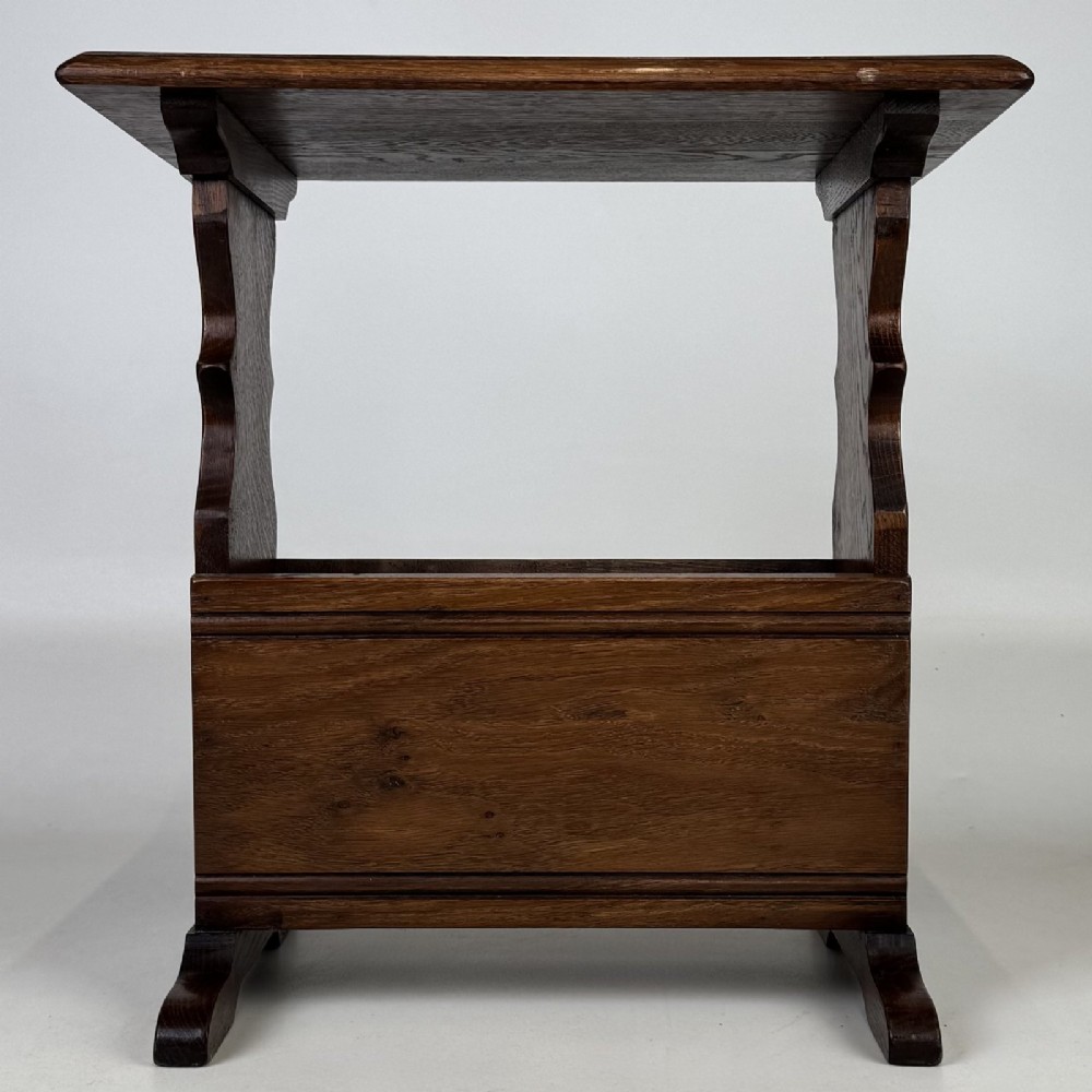 A dark brown oak side table featuring a flat rectangular top supported by shaped vertical legs and a lower integrated magazine compartment.