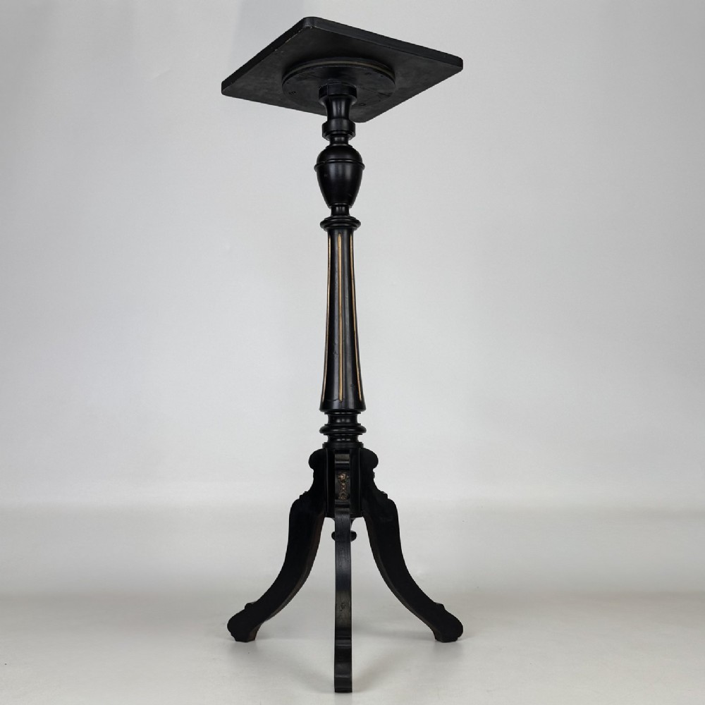 A tall Victorian ebonised wooden plant stand featuring a square top, turned fluted column with gilt highlights, and a curved tripod base.