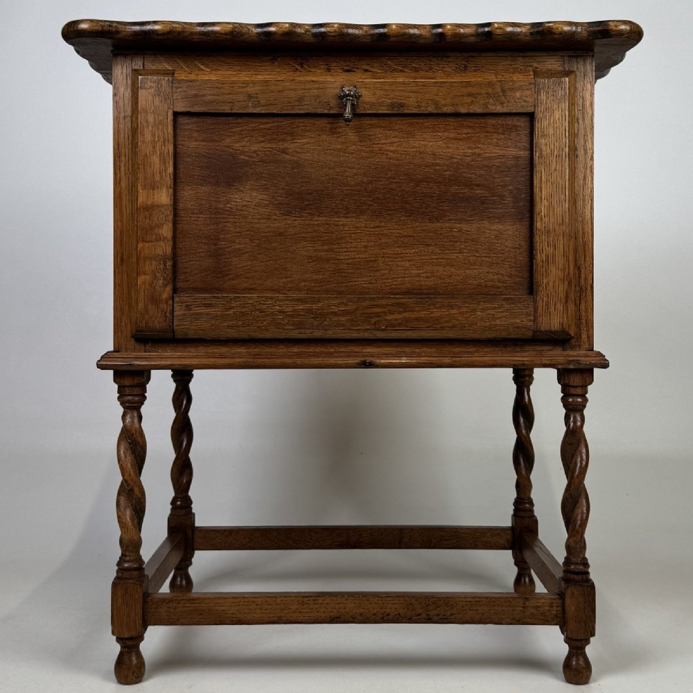 An Edwardian oak side cabinet featuring a single panelled door, a scalloped edge top, and four barley twist legs joined by a lower stretcher.