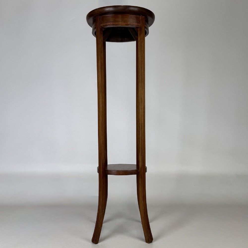 A tall Edwardian mahogany plant stand featuring a circular top, long slender legs, and a small circular lower shelf.