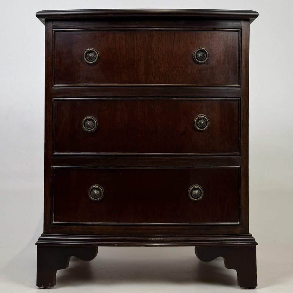 A dark mahogany small chest of three drawers featuring brass ring pull handles and bracket feet.
