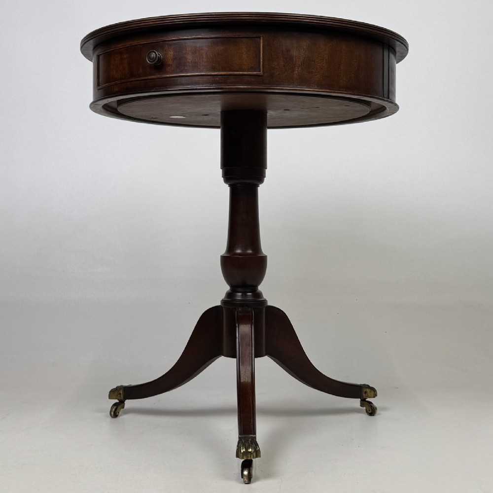 An Edwardian mahogany drum table featuring a circular top with a frieze drawer, supported by a turned pedestal and tripod swept legs on brass claw castors.